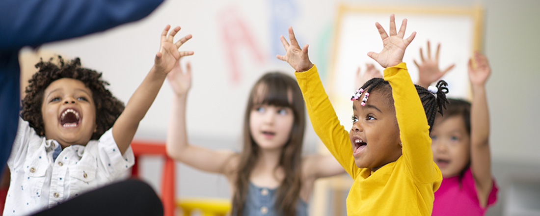 Preschool children raising hands in classroom.